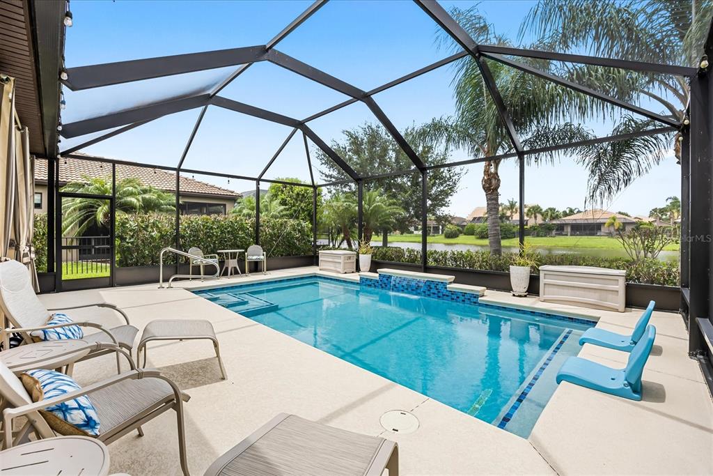 A screened-in patio features a swimming pool with a water feature overlooking a lake — 218 SE LONGVIEW DRIVE, PORT ST LUCIE, FL