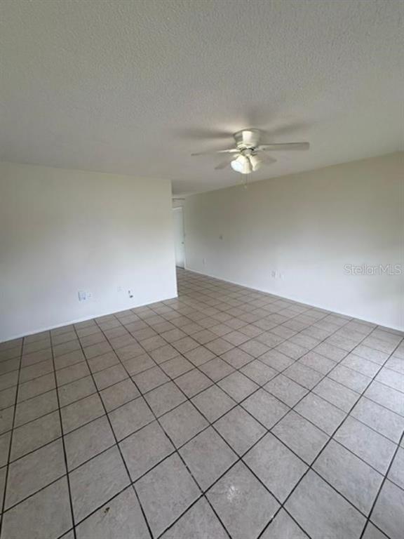 An empty room features white walls, a ceiling fan, and light-colored square floor tiles — 7238 EXEMPLAR DRIVE, NEW PORT RICHEY, FL