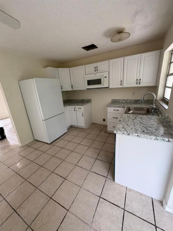 A kitchen features white cabinets, granite countertops, a white refrigerator, and light-colored tile flooring — 7238 EXEMPLAR DRIVE, NEW PORT RICHEY, FL