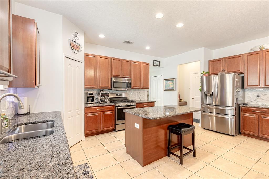A kitchen features wood cabinets, granite countertops, stainless steel appliances, and a central island — 3968 SUNSET COVE DRIVE, PORT ORANGE, FL