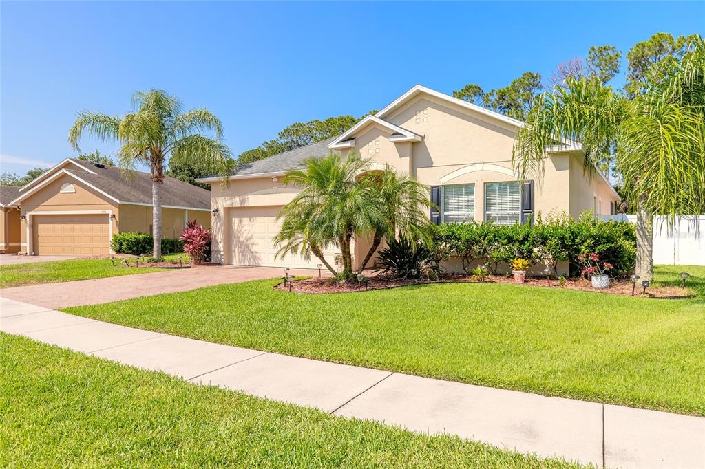 A single-story suburban house with a tan stucco exterior, a two-car garage, and palm trees — 3968 SUNSET COVE DRIVE, PORT ORANGE, FL