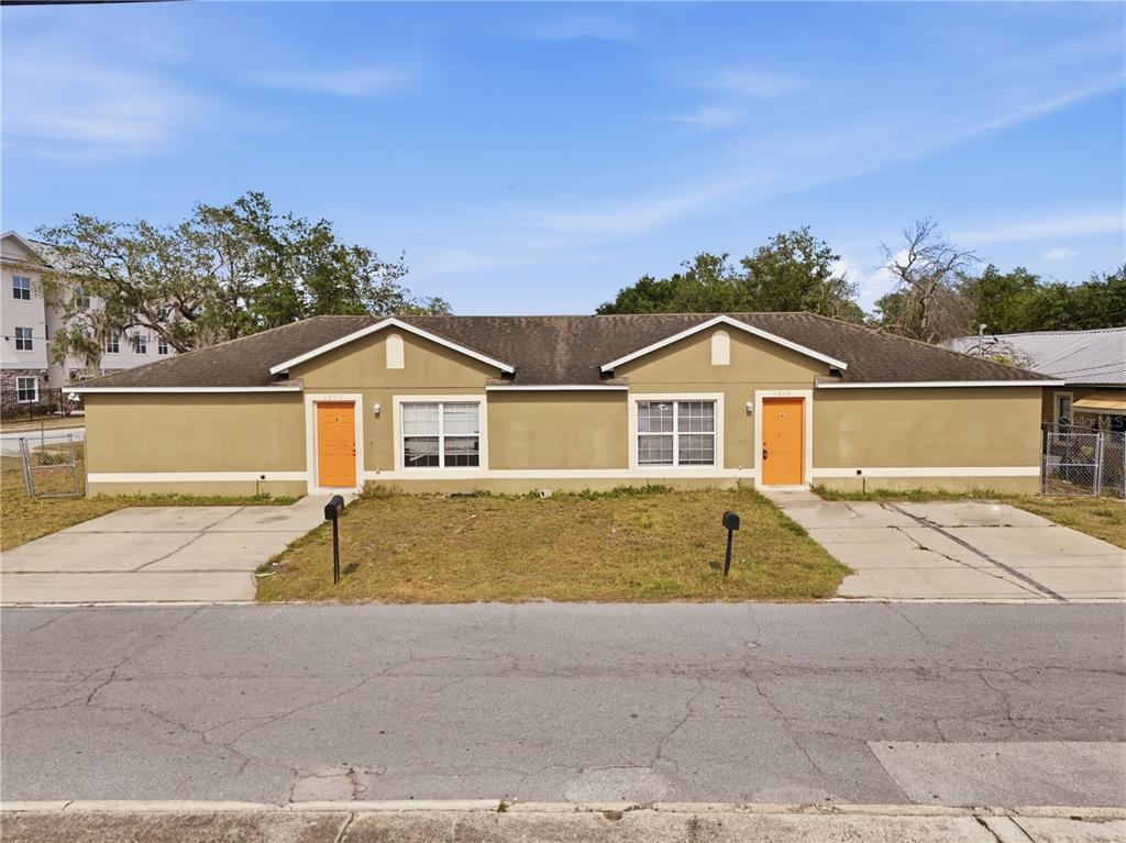 A single-story duplex with tan stucco walls, orange front doors, and two concrete driveways — 1830 2ND STREET NW UNIT A, WINTER HAVEN, FL