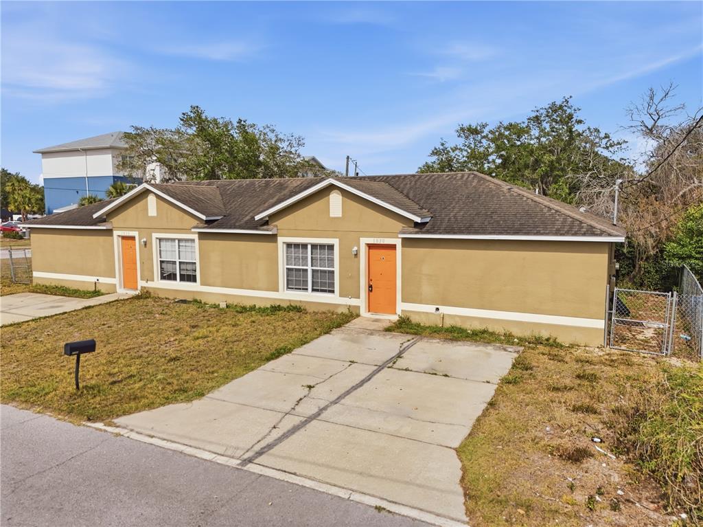 A single-story duplex with tan stucco walls, two orange doors, and a concrete driveway — 1830 2ND STREET NW UNIT A, WINTER HAVEN, FL