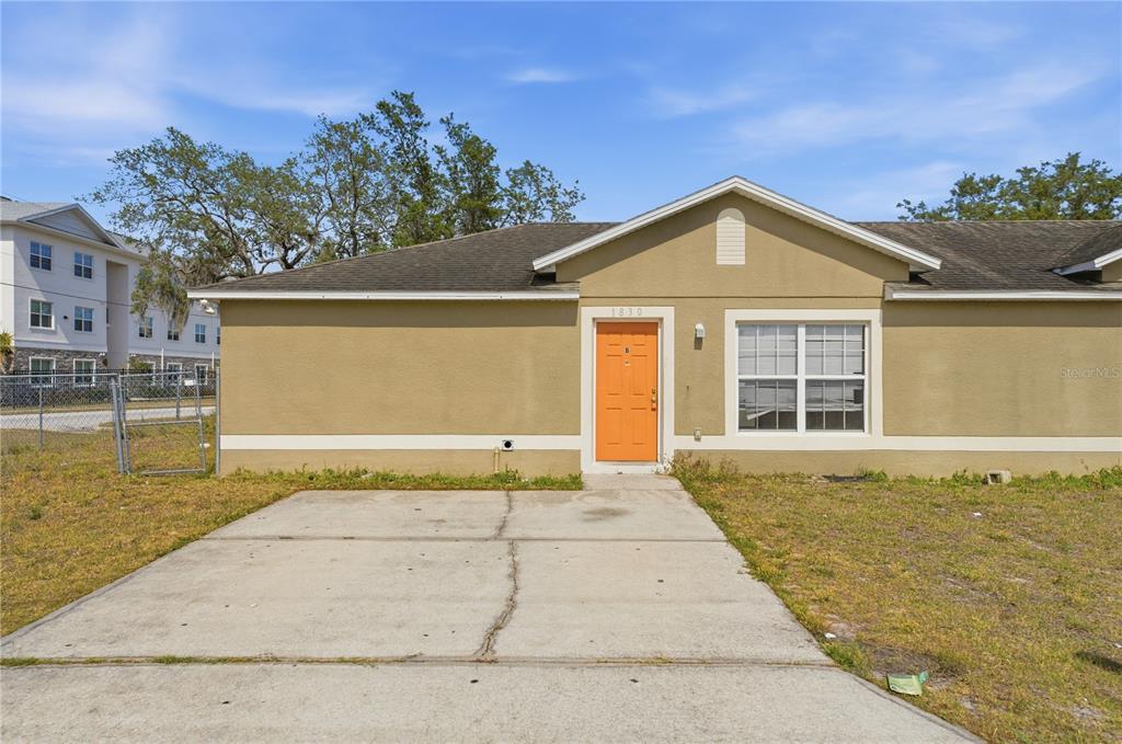 A single-story tan house features an orange front door and a concrete driveway — 1830 2ND STREET NW UNIT A, WINTER HAVEN, FL