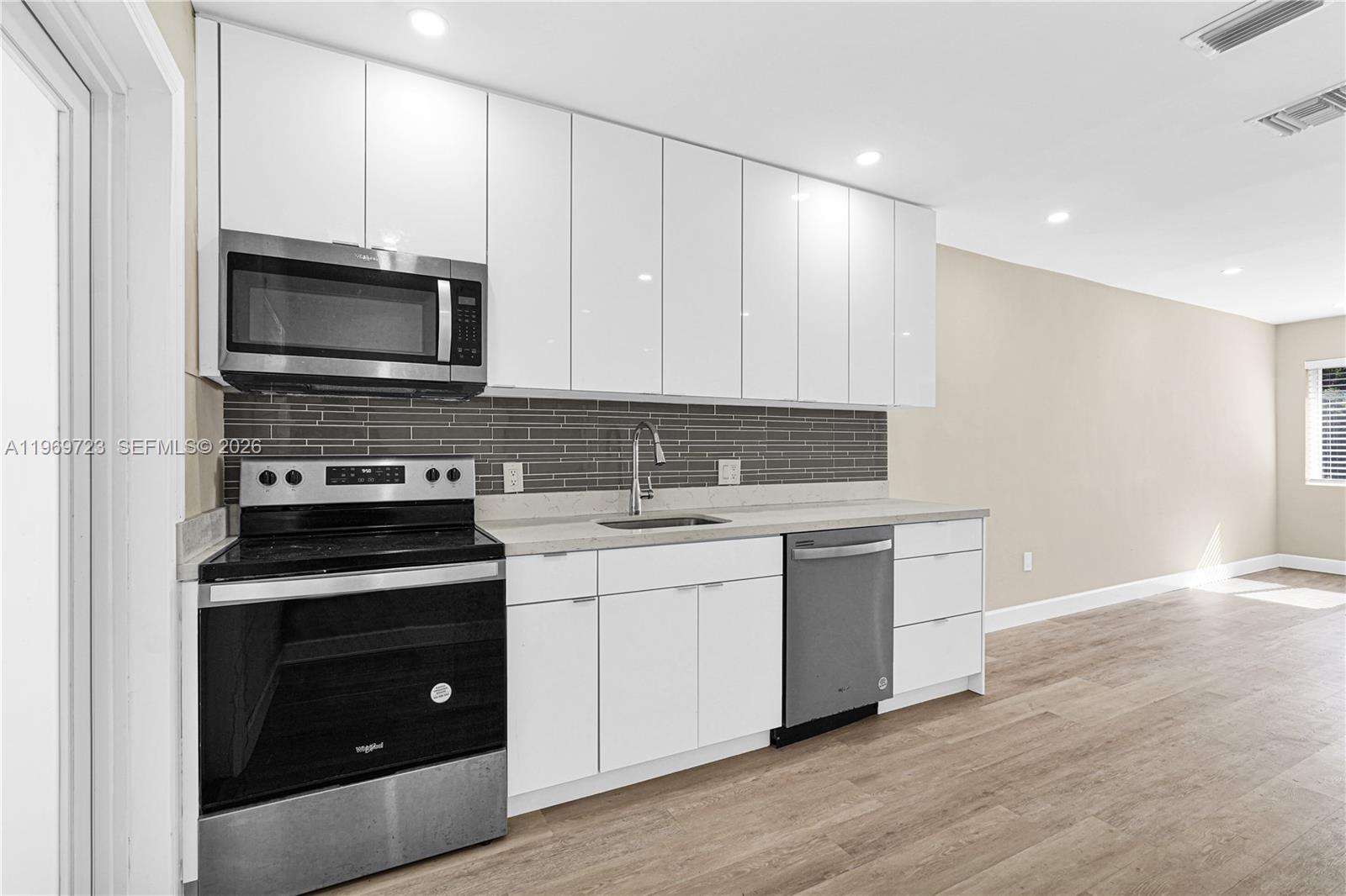 A modern kitchen features white cabinets, stainless steel appliances, and a gray tiled backsplash — 11919 NE 8th Ave, Biscayne Park FL 33161, BISCAYNE PARK, FL