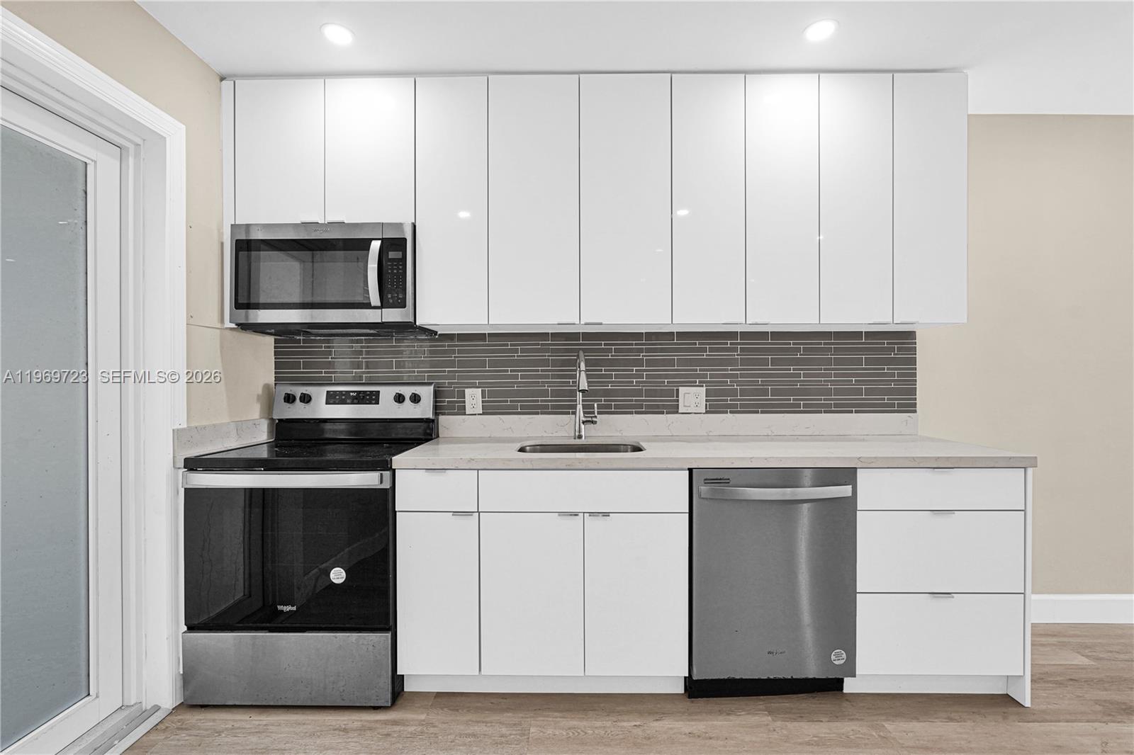 A modern kitchen features white cabinets, stainless steel appliances, and a gray tiled backsplash — 11919 NE 8th Ave, Biscayne Park FL 33161, BISCAYNE PARK, FL
