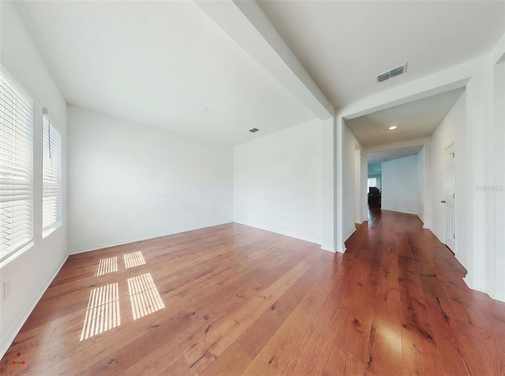 An empty room with white walls, hardwood floors, and a hallway leading to another room — 6084 CLAYSTONE WAY, MOUNT DORA, FL