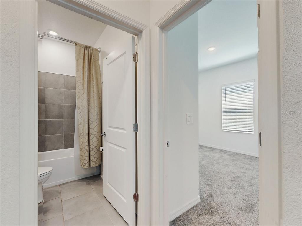 A view through two doorways showing a tiled bathroom and a carpeted bedroom — 6084 CLAYSTONE WAY, MOUNT DORA, FL