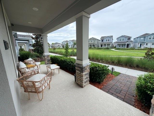 A covered front porch features wicker chairs and stone-based columns overlooking a suburban neighborhood — 1704 FRIENDSHIP ROW, KISSIMMEE, FL