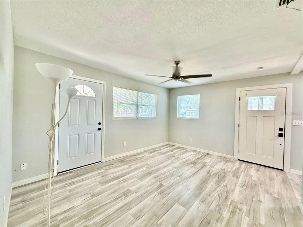 An empty room features light gray walls, wood-look flooring, a ceiling fan, and two doors — 4406 W TRILBY AVENUE, TAMPA, FL