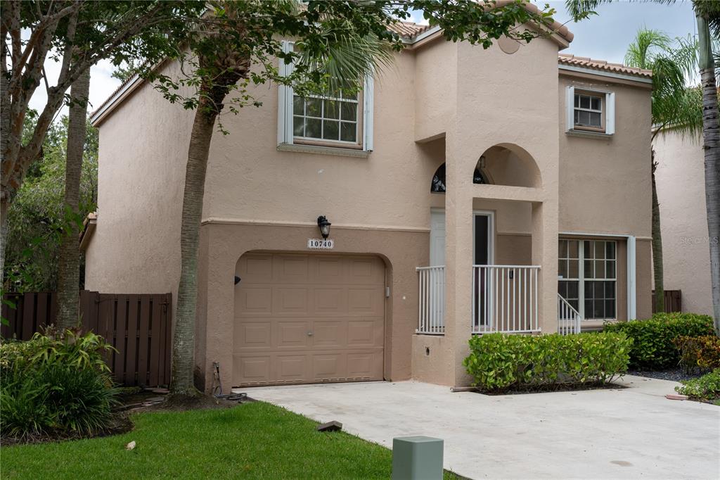 A two-story tan stucco house with a single-car garage and a small front porch — 10740 NW 12TH MANOR, PLANTATION, FL