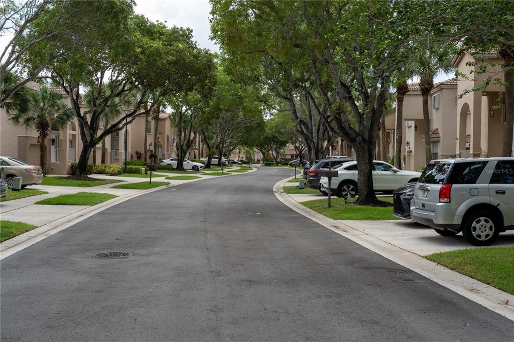 A paved residential street lined with townhouses, mature trees, and parked cars — 10740 NW 12TH MANOR, PLANTATION, FL