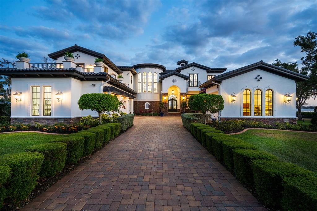 A large, two-story white stucco house with a brick driveway and manicured hedges at dusk — 2107 4TH STREET COURT W, PALMETTO, FL