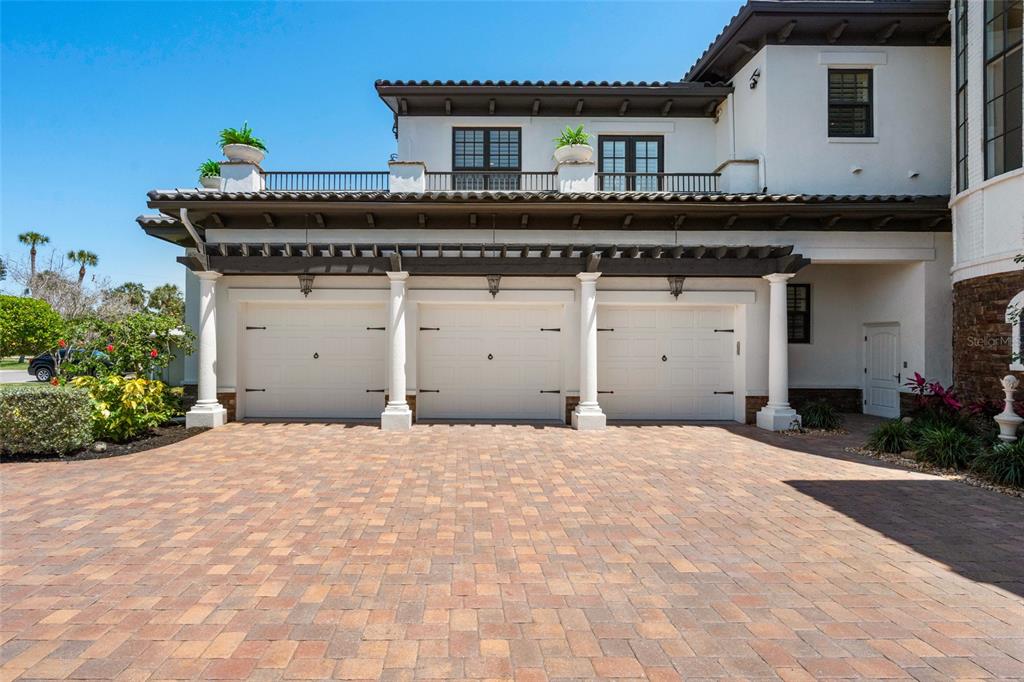 A three-car garage with a pergola and a balcony above sits behind a brick driveway — 2107 4TH STREET COURT W, PALMETTO, FL