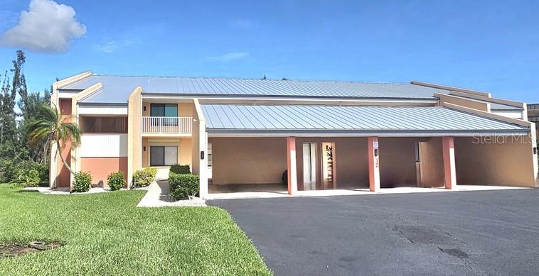A two-story building features a metal roof, covered parking bays, and a grassy lawn — 1354 ROCK DOVE COURT UNIT A203, PUNTA GORDA, FL