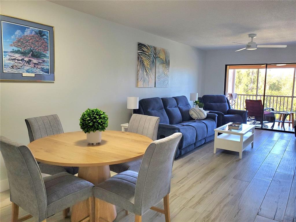 A living and dining room with wood-look tile floors, blue furniture, and a balcony view — 1354 ROCK DOVE COURT UNIT A203, PUNTA GORDA, FL