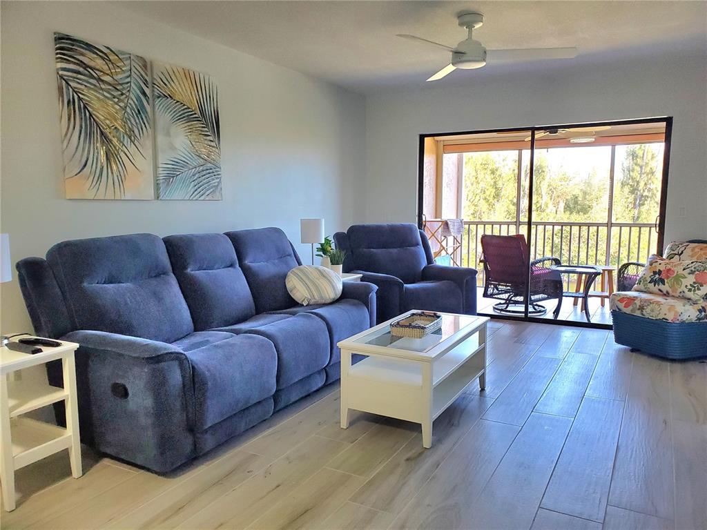 A living room features a blue sofa, matching recliner, white coffee table, and balcony access — 1354 ROCK DOVE COURT UNIT A203, PUNTA GORDA, FL