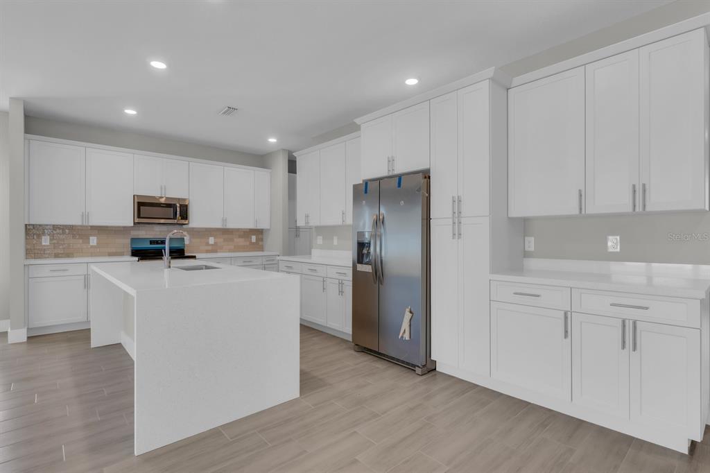 A modern kitchen features white cabinetry, a large quartz island, and stainless steel appliances — 1811 MISSOURI ROAD NW, PALM BAY, FL
