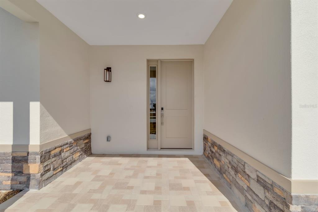 A covered entryway features stone veneer siding, a paved floor, and a modern front door — 1811 MISSOURI ROAD NW, PALM BAY, FL