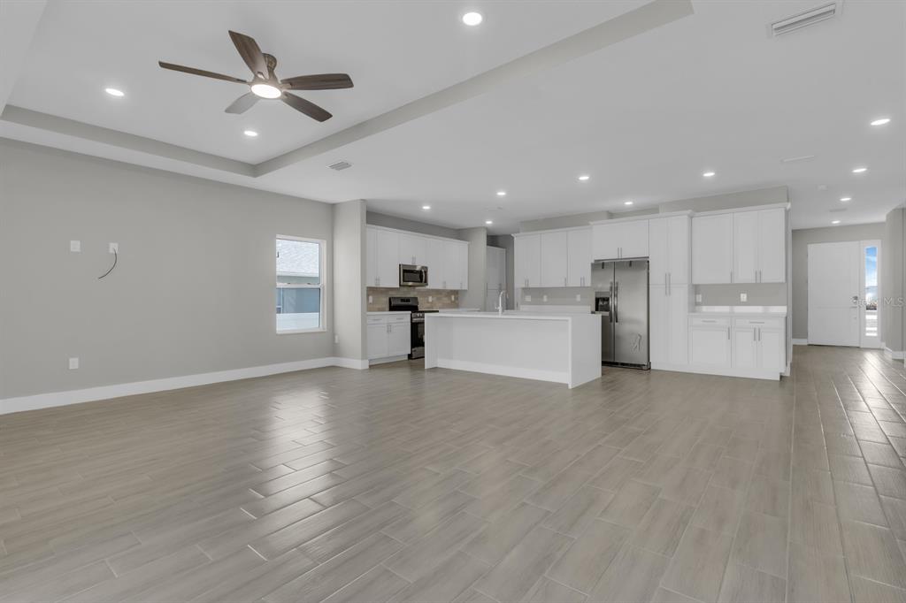 An open-concept kitchen and living area features white cabinetry, a central island, and tile flooring — 1811 MISSOURI ROAD NW, PALM BAY, FL