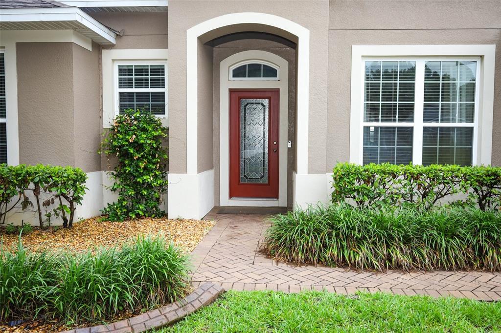 A red front door with a glass insert sits under an arched entryway of a house — 1661 BLUE GRASS BOULEVARD, DELAND, FL