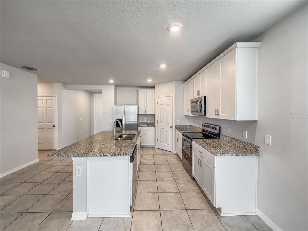 A kitchen features white cabinets, granite countertops, a center island, and tile flooring — 868 TETON STREET, HAINES CITY, FL