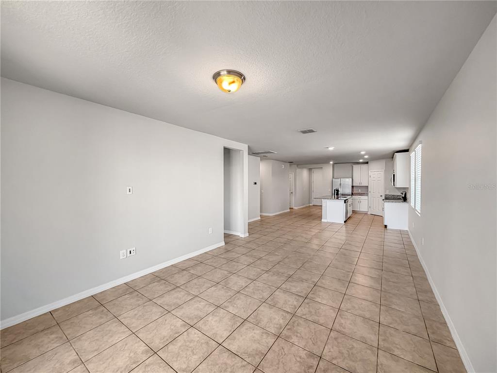 An open-concept living area features light-colored walls, tile flooring, and a kitchen in the background — 868 TETON STREET, HAINES CITY, FL