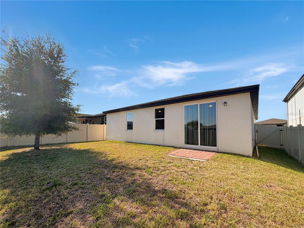 A view of a backyard featuring a beige house exterior, a sliding glass door, and fencing — 868 TETON STREET, HAINES CITY, FL
