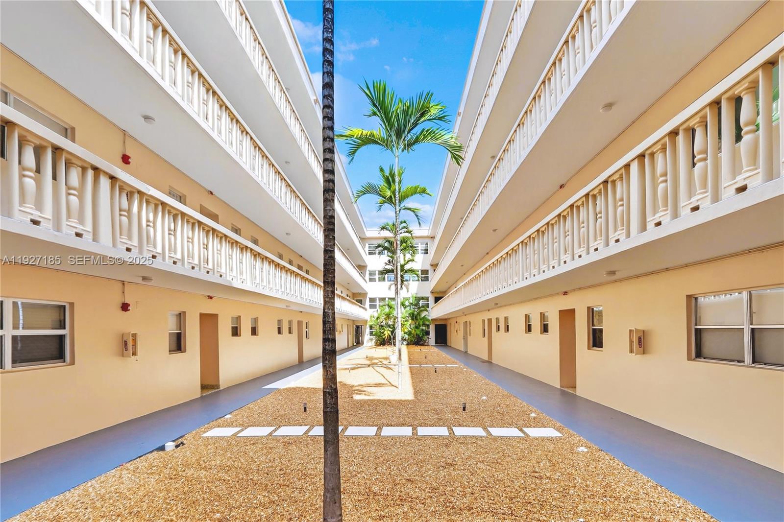 An outdoor courtyard features a gravel path, palm trees, and two-story apartment building wings — 410 SE 2nd St # 111, Hallandale Beach FL 33009, HALLANDALE BEACH, FL