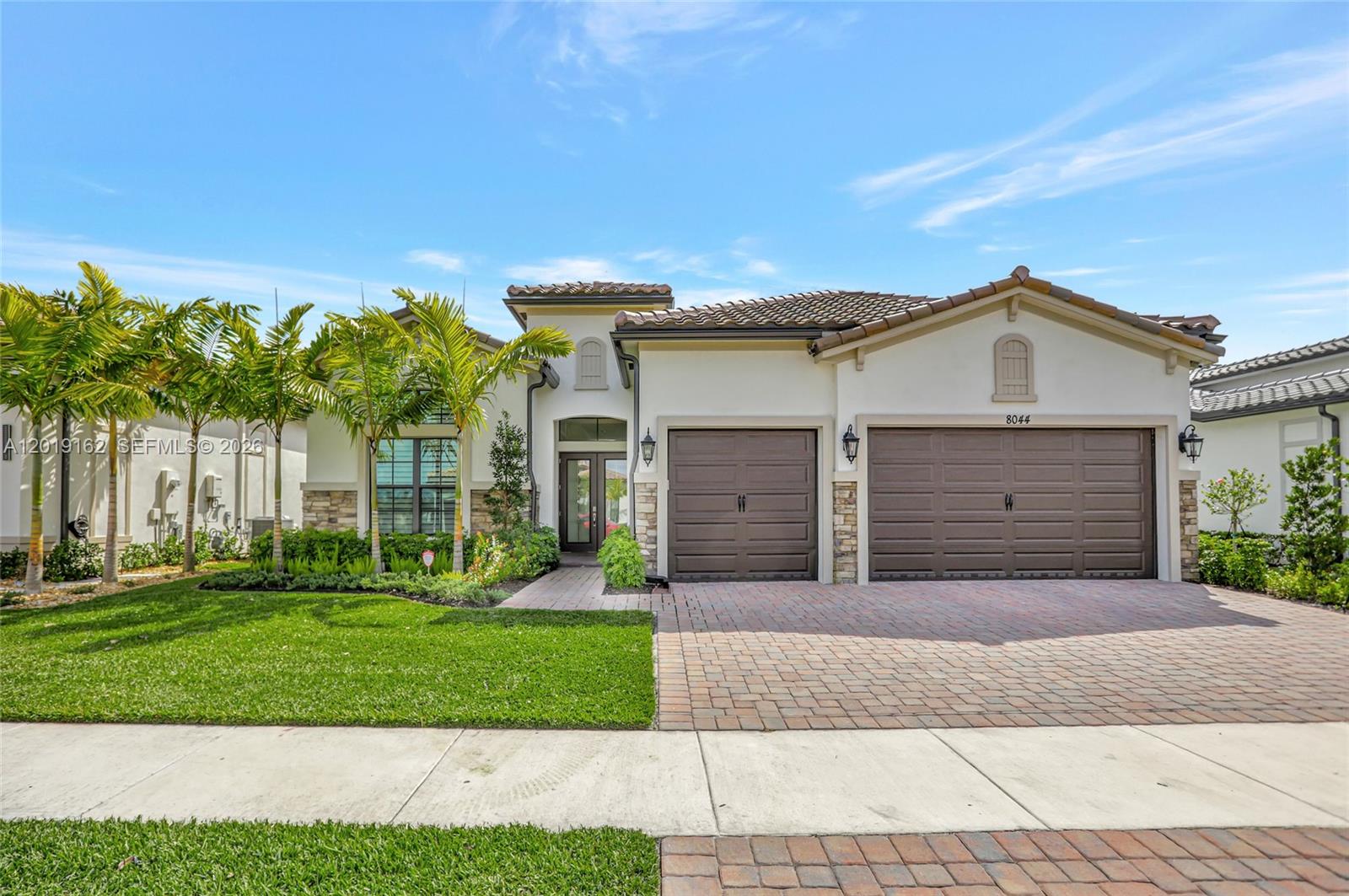 A single-story house with a three-car garage, brick paver driveway, and palm trees — 8044 Ironwood Way, Parkland FL 33067, PARKLAND, FL