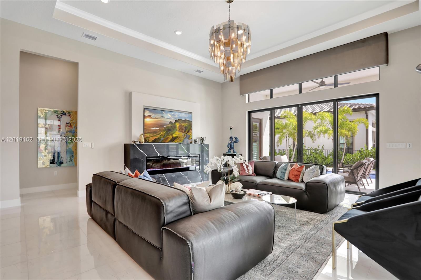 A modern living room features a black marble fireplace, leather sofas, and a large chandelier — 8044 Ironwood Way, Parkland FL 33067, PARKLAND, FL