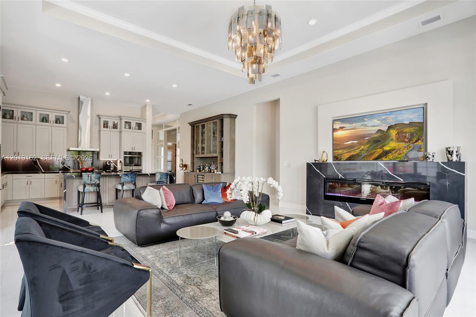 A modern living room features a black marble fireplace, leather sofas, and an open kitchen — 8044 Ironwood Way, Parkland FL 33067, PARKLAND, FL