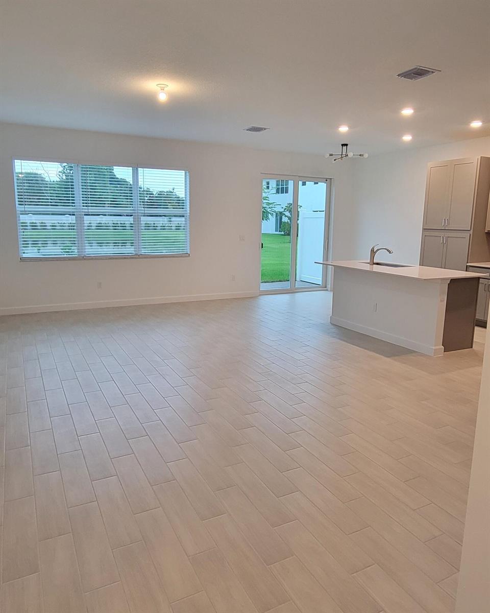 An open-concept living area features light wood-look tile flooring, a kitchen island, and sliding doors — 4946 Navali Drive, Lake Worth FL 33467, LAKE WORTH, FL