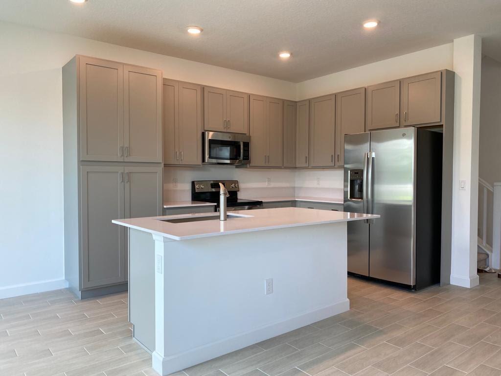 A modern kitchen features gray cabinets, a white island, stainless steel appliances, and tile flooring — 4946 Navali Drive, Lake Worth FL 33467, LAKE WORTH, FL