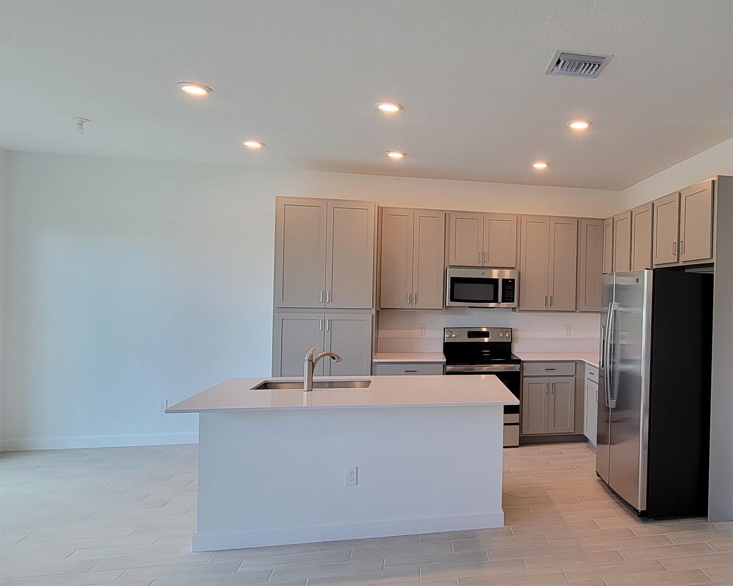 A modern kitchen features light gray cabinets, stainless steel appliances, and a white island countertop — 4946 Navali Drive, Lake Worth FL 33467, LAKE WORTH, FL