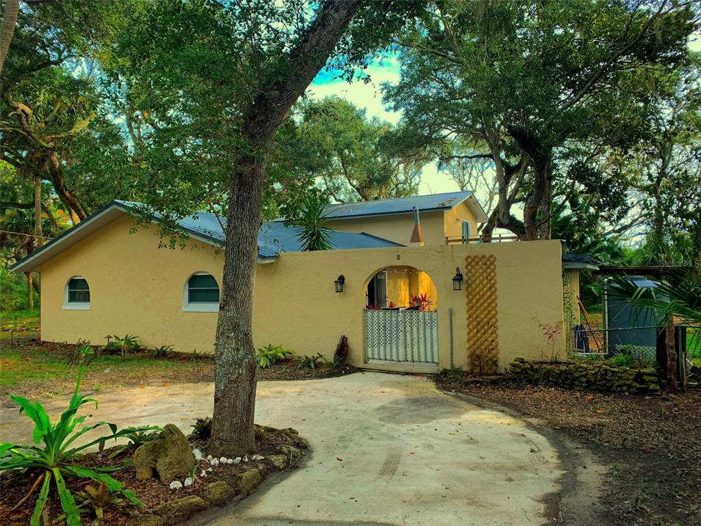 A yellow house with a gated courtyard entrance sits behind a concrete driveway and trees — 3 ELIZABETH DRIVE E, PALM COAST, FL