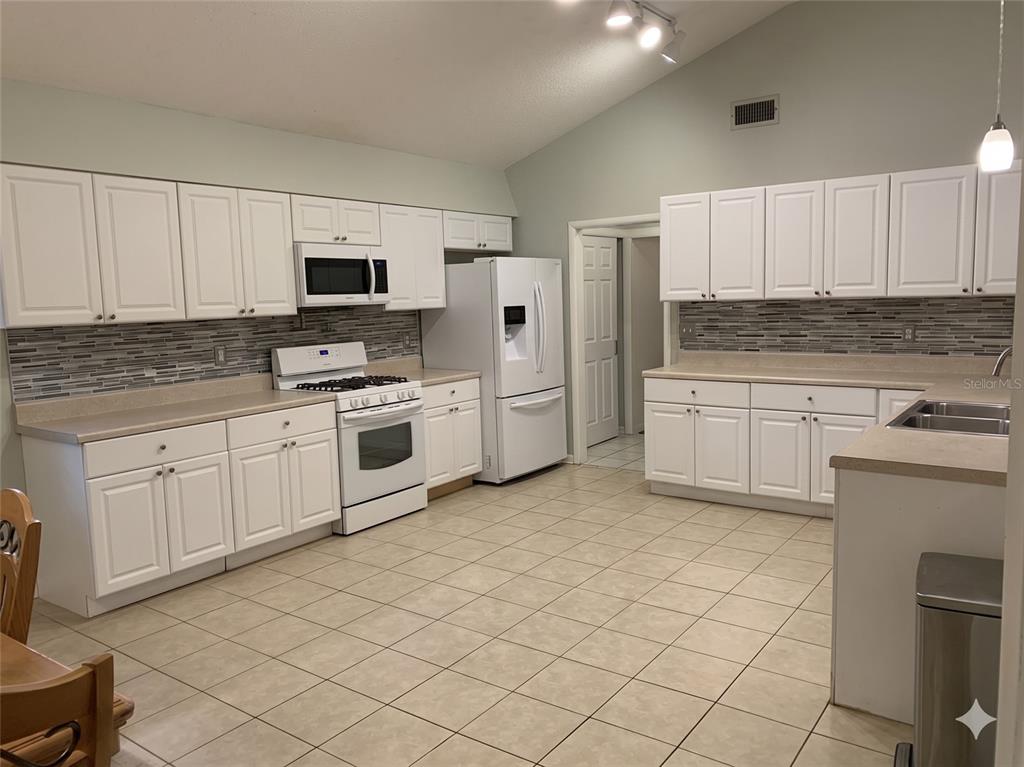 A kitchen features white cabinetry, tan countertops, a tile backsplash, and white appliances — 3 ELIZABETH DRIVE E, PALM COAST, FL