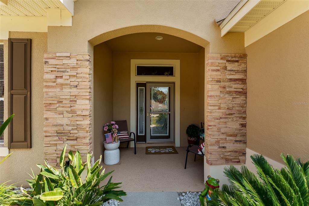 A covered front entryway features stone-accented columns, a glass storm door, and potted plants — 10501 VIA COMO COURT, CLERMONT, FL
