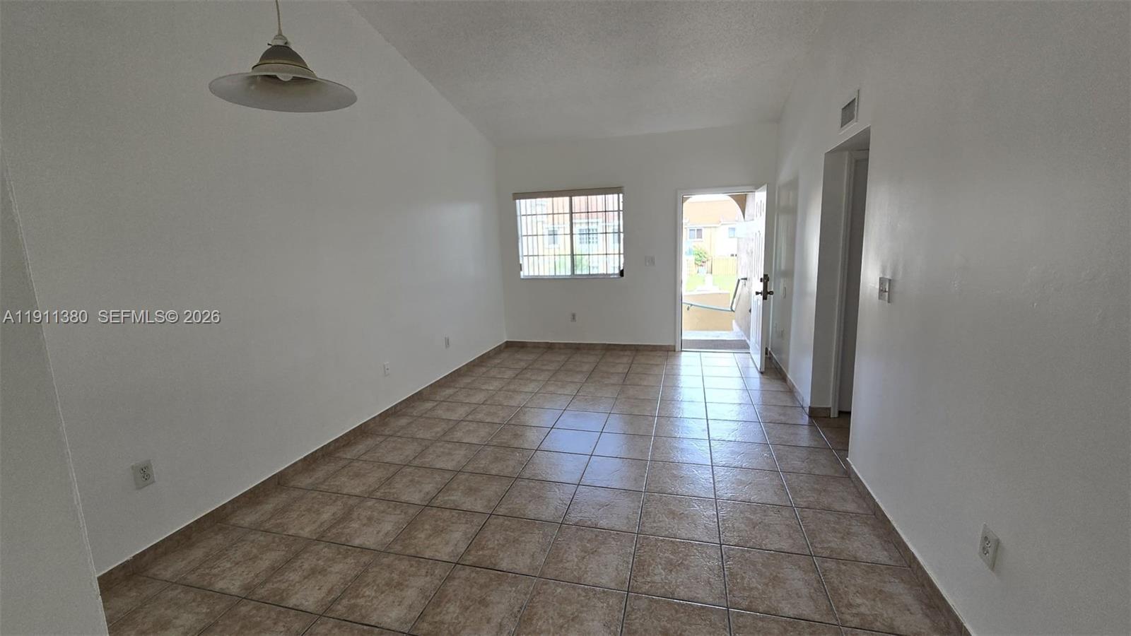 An empty room with white walls, tile flooring, a single pendant light, and an exterior door — 13120 SW 64th Ter # 1510, Miami FL 33183, MIAMI, FL