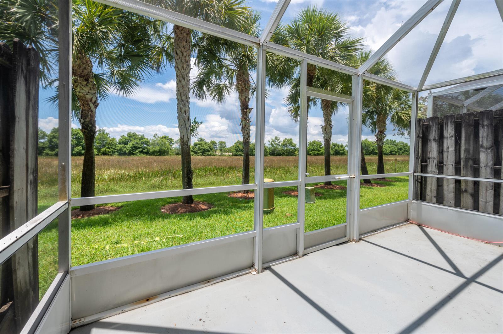 A screened-in patio overlooks a grassy yard with palm trees and a field — 2391 Pasadena Way, Weston FL 33327, WESTON, FL