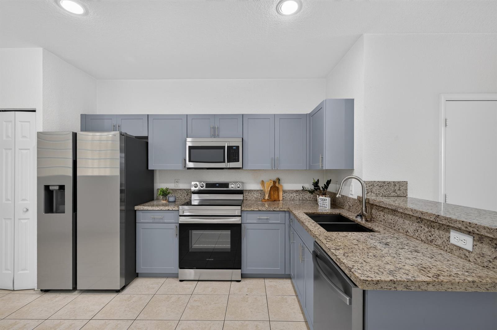 A kitchen features blue cabinets, granite countertops, stainless steel appliances, and light-colored tile flooring — 2391 Pasadena Way, Weston FL 33327, WESTON, FL