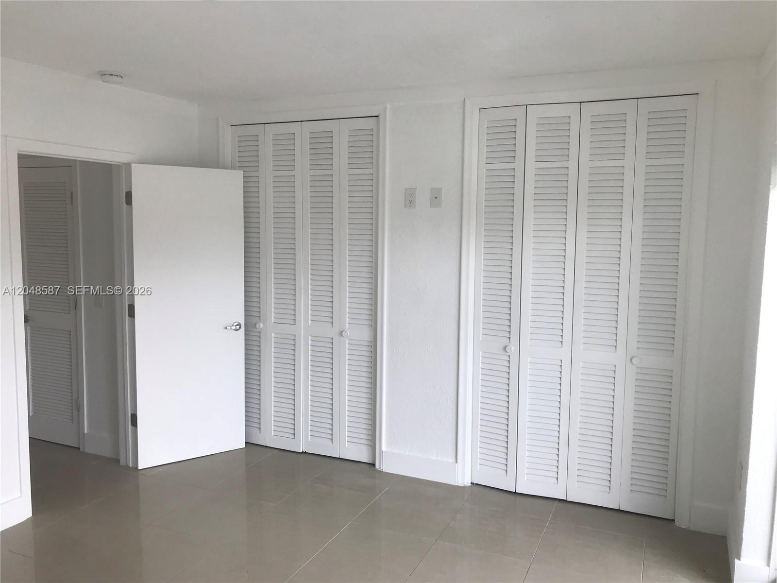 A room with light tile flooring, white walls, and two sets of white louvered closet doors — 2185 NE 123rd St # 208, North Miami FL 33181, NORTH MIAMI, FL