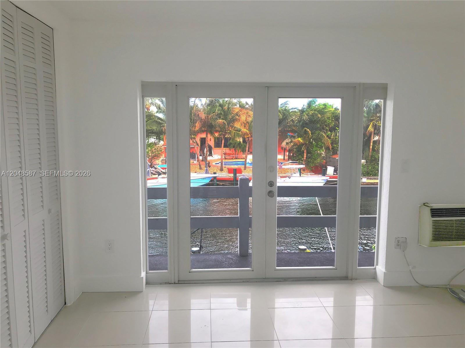 A room with white tile floors and louvered closet doors overlooks a canal with boats — 2185 NE 123rd St # 208, North Miami FL 33181, NORTH MIAMI, FL
