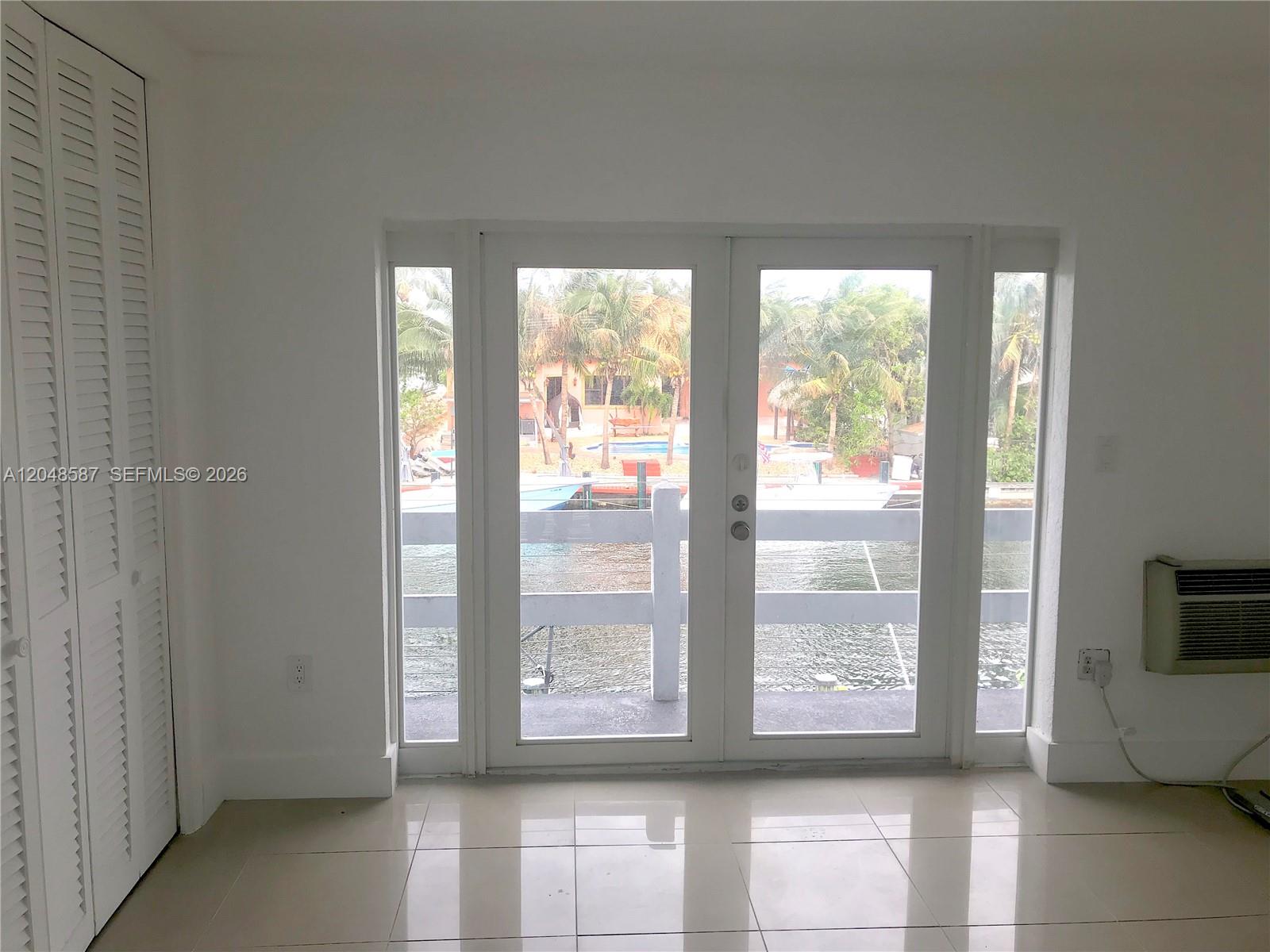 A room with white walls, tiled floors, louvered closet doors, and glass doors overlooking water — 2185 NE 123rd St # 208, North Miami FL 33181, NORTH MIAMI, FL