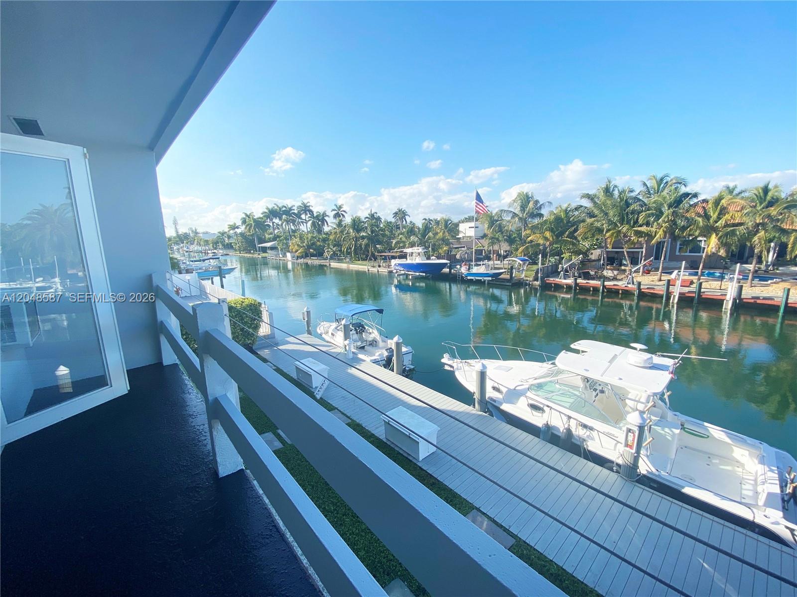 A balcony overlooks a canal with docked boats and palm trees under a clear sky — 2185 NE 123rd St # 208, North Miami FL 33181, NORTH MIAMI, FL