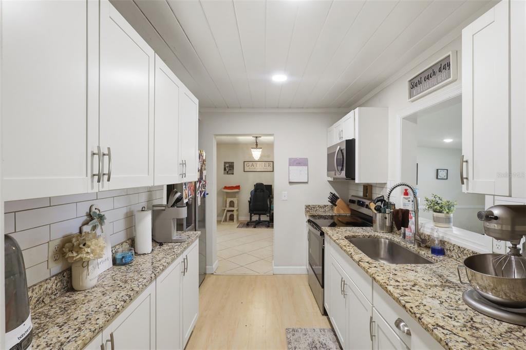 A galley kitchen features white cabinets, granite countertops, a stainless steel sink, and subway tile — 112 EDWARDS AVENUE, ORANGE CITY, FL