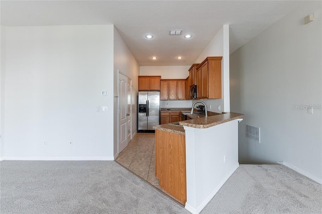 A kitchen with wood cabinets, stainless steel appliances, and a breakfast bar overlooks a carpeted room — 6612 S GOLDENROD ROAD UNIT 104A, ORLANDO, FL