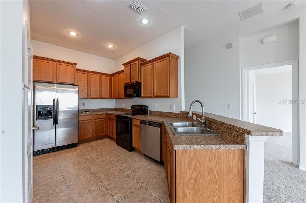 A kitchen features wood cabinets, stainless steel appliances, a laminate countertop, and tile flooring — 6612 S GOLDENROD ROAD UNIT 104A, ORLANDO, FL