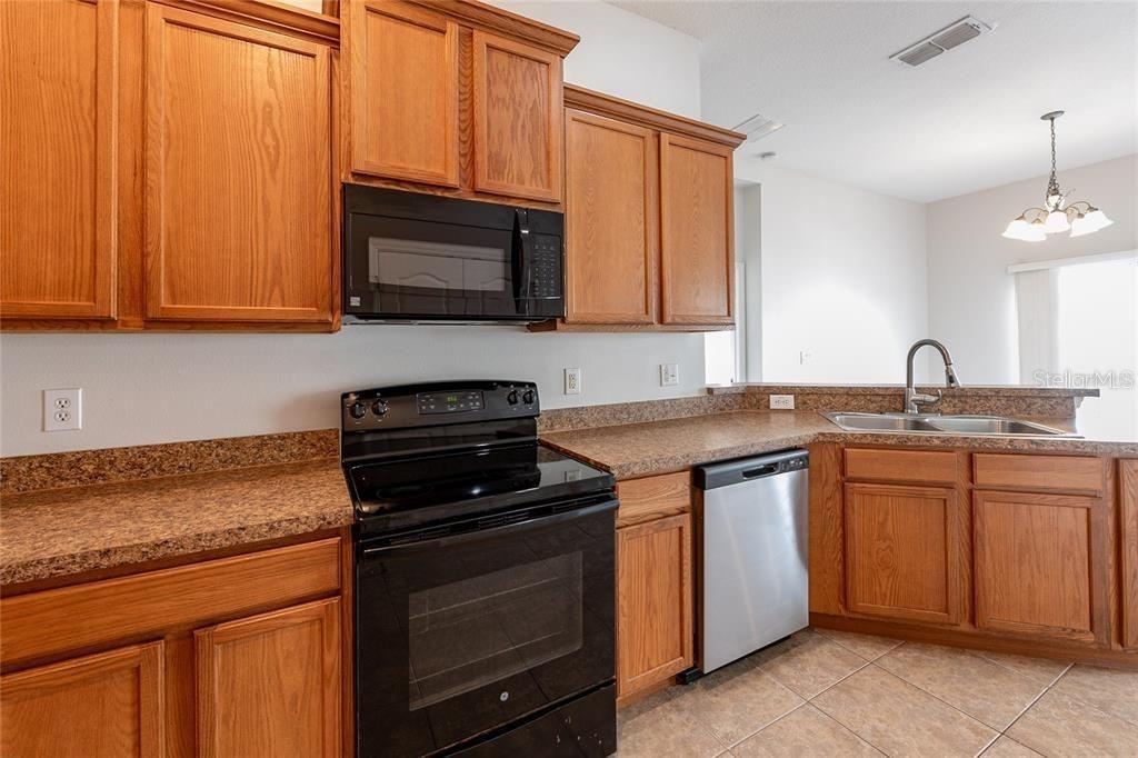 A kitchen features oak cabinets, granite-look laminate countertops, and black appliances — 6612 S GOLDENROD ROAD UNIT 104A, ORLANDO, FL