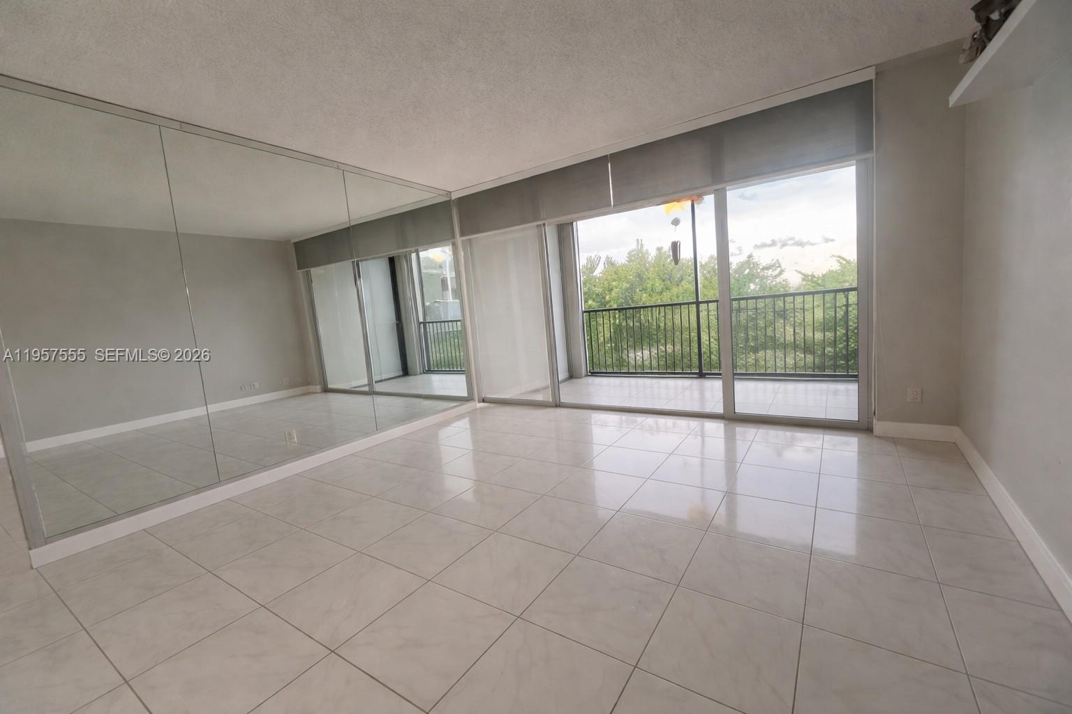 A room with light-colored tile flooring, a mirrored wall, and a sliding glass door to a balcony — 3910 Inverrary Blvd # B, Lauderhill FL 33319, LAUDERHILL, FL